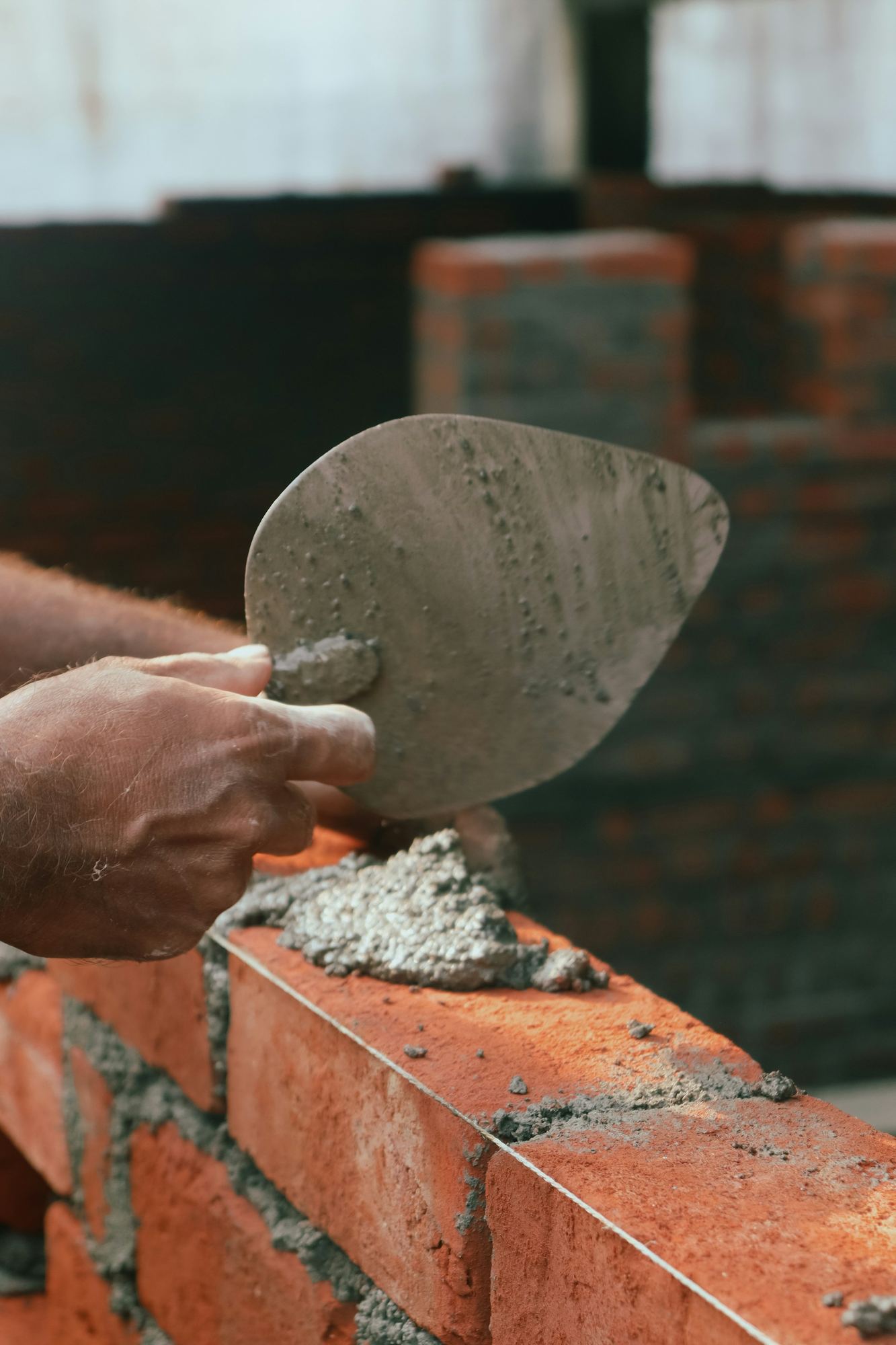Close-up of a trowel spreading mortar on a course of red bricks