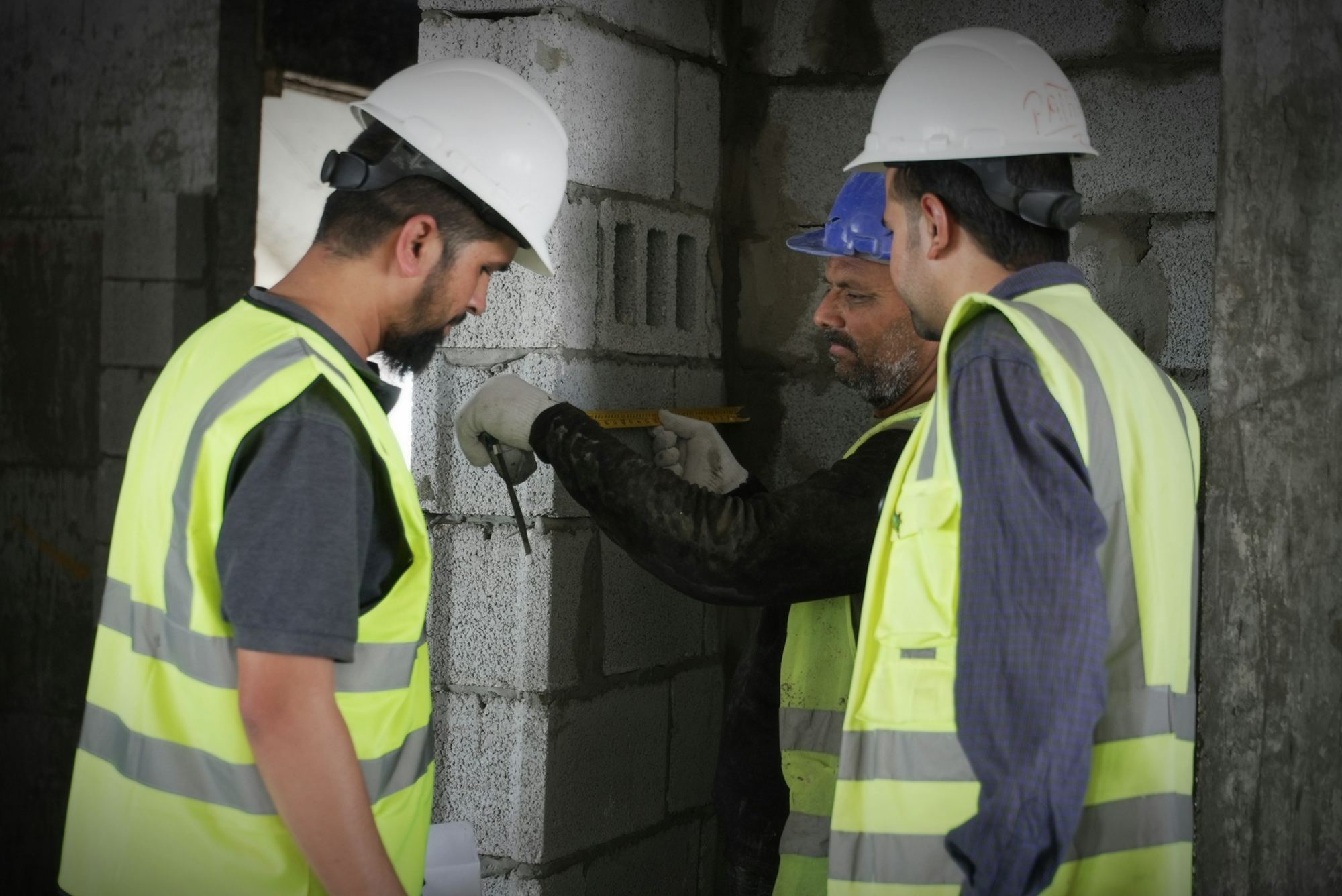 Two builders in hard hats and hi-vis vests checking a blockwork wall